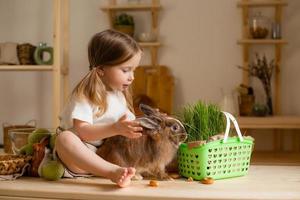 süß wenig Mädchen im das hölzern Küche von das Haus Einspeisungen das Hase frisch Gras foto