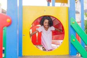 dunkel Baby mit lockig Haar im ein blass Rosa Kleid Theaterstücke auf ein Straße Spielplatz und Fahrten Nieder das hügel. das Konzept von ein gesund Lebensstil. glücklich Kindheit. hoch Qualität Foto