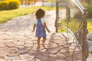 Porträt wenig glücklich spielerisch Kleinkind dunkel Mädchen im ein Denim Sommerkleid Stehen im das Garten auf ein sonnig Tag. Gehen im das frisch Luft. Konzept von ein glücklich Kindheit. Raum zum Text. hoch Qualität Foto