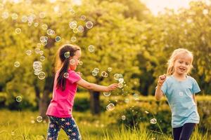 zwei Mädchen sind glücklich Über das schwebend Seife Luftblasen im Natur foto