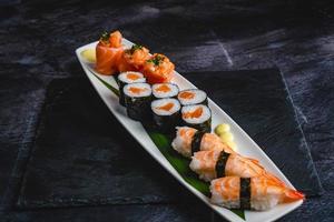 ein Weiß Teller gekrönt mit Sushi auf oben von ein schwarz Tisch, verdrehte Formen, drei Türme, lange fließend Flossen. foto