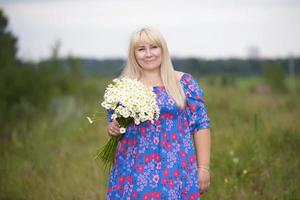 schön Plus Größe Frau mit Weiß Haar im ein Sommer- Kleid posieren draußen mit Gänseblümchen. mollig Mädchen im ein Wiese mit Blumen. foto