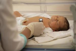 Neonatologie. Arzt Hören zu das Herzschlag von ein Neugeborene im ein Säugling Inkubator foto