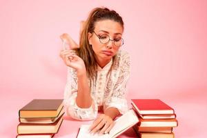 Rosa Hintergrund, ein Mädchen liest Bücher, ein Buch Liebhaber, ein Schüler Lügen auf das Fußboden unter ein groß Nummer von Bücher foto