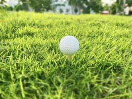 golfball nah oben auf grünem gras auf unscharfer schöner landschaft des golfplatzes mit sonnenaufgang, sonnenuntergangszeit auf hintergrund.konzept internationaler sport, der auf präzisionsfähigkeiten zur gesundheitsentspannung angewiesen ist. foto