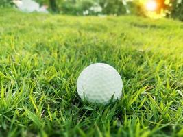 golfball nah oben auf grünem gras auf unscharfer schöner landschaft des golfplatzes mit sonnenaufgang, sonnenuntergangszeit auf hintergrund.konzept internationaler sport, der auf präzisionsfähigkeiten zur gesundheitsentspannung angewiesen ist. foto