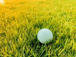 golfball nah oben auf grünem gras auf unscharfer schöner landschaft des golfplatzes mit sonnenaufgang, sonnenuntergangszeit auf hintergrund.konzept internationaler sport, der auf präzisionsfähigkeiten zur gesundheitsentspannung angewiesen ist. foto