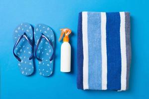 oben Aussicht von Strand eben legen Zubehör. Sonnenschutz Flasche mit Handtuch und Flip Flops auf Blauer Hintergrund mit Kopieren Raum foto