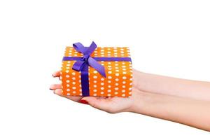 Frauenhände geben eingewickeltes Weihnachts- oder anderes handgemachtes Weihnachtsgeschenk in orangefarbenem Papier mit lila Schleife. isoliert auf weißem Hintergrund, Ansicht von oben. Thanksgiving-Geschenkbox-Konzept foto