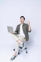 jung asiatisch Geschäft Mann Sitzung auf Stuhl und mit Laptop auf Hintergrund foto