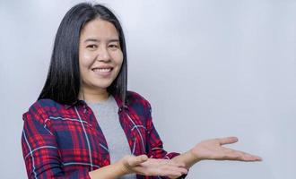 Porträt von Erwachsene asiatisch Dame lächelnd mit heiter Ausdruck, zeigt an etwas tolle beim leer Raum im beiläufig Kleidung und Stehen isoliert Über grau Hintergrund. Gesichts- Ausdruck Konzept. foto