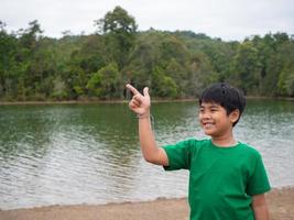 Der Junge lächelte und deutete mit der Hand auf seine Seite. im Hintergrund ist ein Reservoir. foto