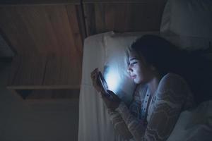 asiatische frau, die nachts auf dem smartphone im bett spielt, thailänder, süchtige soziale medien foto