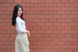 Porträt eines Hipster-Mädchens auf Backsteinmauerhintergrund, schöne asiatische Frauenpose für ein Foto, Kawaii-Stil foto