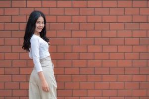 Porträt eines Hipster-Mädchens auf Backsteinmauerhintergrund, schöne asiatische Frauenpose für ein Foto, Kawaii-Stil foto
