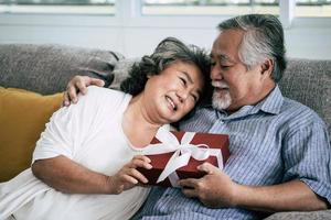 älteres Ehepaar überrascht mit Geschenkbox im Wohnzimmer