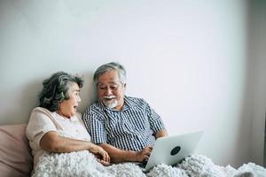 älteres Ehepaar spricht und benutzt Laptop im Schlafzimmer