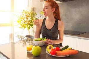 sportlich jung rot behaart Frau im das Zuhause Küche Essen ein gesund Salat foto