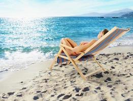 Mädchen bräunt auf ein Deck Stuhl auf ein schön Strand foto