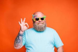 Fett glücklich Mann mit Bart, Tätowierungen und Sonnenbrille ist bereit zum das Sommer- foto