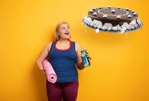 Fett Mädchen denkt zu Essen Süßigkeiten stattdessen von tun Fitnessstudio. Gelb Hintergrund foto