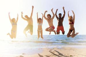 glücklich lächelnd freunde Springen beim das Strand foto