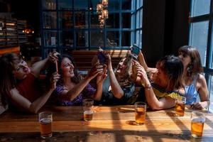 Gruppe von lächelnd weiblich freunde nehmen ein Selfie mit ein Smartphone während Trinken Bier im ein Kneipe foto