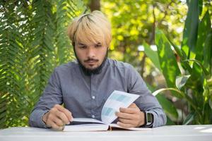 bärtiger Mann des jungen Hipsters, der Bücher im Hausgarten mit Natur liest
