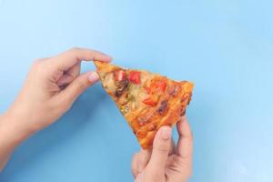 Hand hält ein Stück Pizza auf blauem Hintergrund foto