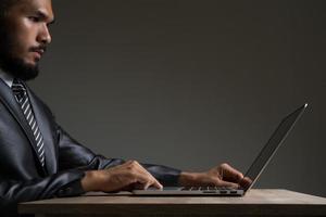 junger Geschäftsmann sitzt arbeitend mit Laptop lokalisiert auf schwarzem Hintergrund foto