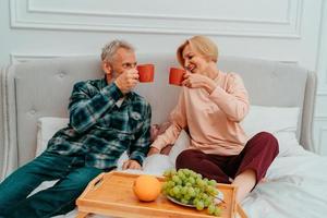 Mann und Ehefrau haben Frühstück auf das Bett mit Kaffee und Obst foto