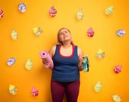 Fett Mädchen denkt zu Essen Süßigkeiten stattdessen von tun Fitnessstudio. Gelb Hintergrund foto