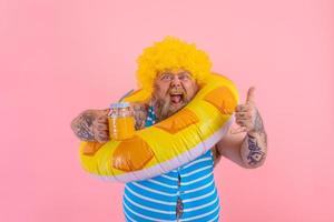 Fett glücklich Mann mit Perücke im Kopf ist bereit zu schwimmen mit ein Krapfen Lebensretter foto