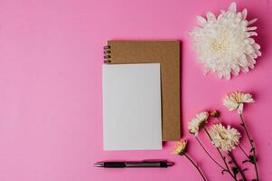 Notizbuch und Karte mit Stift auf Rosa Hintergrund dekoriert mit Blumen foto