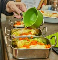 Koch gießt Soße auf Kohl Rollen mit Lachs, Möhren im das Küche. Französisch Rezept foto