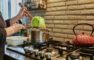 Koch nimmt gekocht Kohl aus von das Topf auf das Gas Herd foto