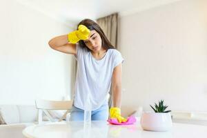 Porträt von jung müde Frau mit Gummi Handschuhe ruhen nach Reinigung ein Wohnung. heim, Hauswirtschaft Konzept. foto
