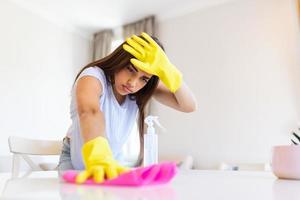 Schuss von ein jung Frau suchen müde während Reinigung beim heim. müde jung Frau Stehen mit Reinigung Produkte und Ausrüstung, Hausarbeit Konzept. foto