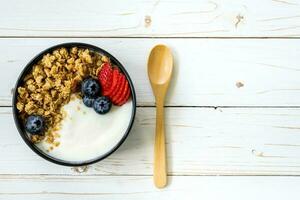 Schüssel von Granola mit Joghurt, frisch Beeren, Erdbeere auf Holz Tisch. foto