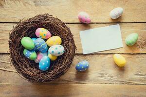 bunt Ostern Ei im Nest und Papier Karte auf Holz Hintergrund mit Raum. foto