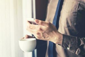 schließen oben Geschäft Mann halten Smartphone und Kaffee im das Büro mit Sonnenlicht. Jahrgang getönt Filter. foto