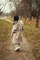 Porträt von Brünette Haar Frau im Beige Mantel Gehen beim das Stadt Park . foto