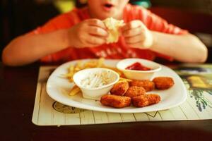 Junge Essen schnell Essen im ein Cafe. das Kind Essen Französisch Fritten mit Nuggets foto