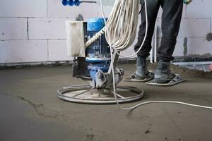 rammen und Mahlen von halb Trocken Fußboden Estrich durch ein Maschine mit ein rotierend Platte zum Nivellierung. Konstruktion von ein Beton Fußboden im das Haus, ein Meister mit Besondere Ausrüstung. foto