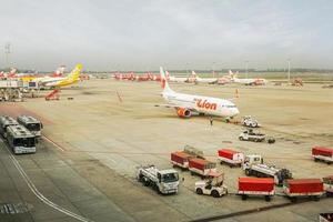 Bangkok, Thailand 2018 Flugzeug Rückschläge Traktor Schleppen das Flugzeug von thailändisch Löwe Luft im Runway mit Ladung Bedienung Karren und Luft Flugzeug geparkt hinter beim Don mueang International Flughafen. foto