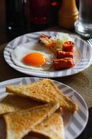 Frühstück, gebraten Eier, gebraten Wurst, Gemüse Salat und Toast auf ein braun hölzern Tabelle mit Kaffee. foto