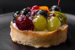 köstlich frisch Torte mit Blaubeeren, Kirschen, Trauben auf ein schwarz Keramik Teller foto