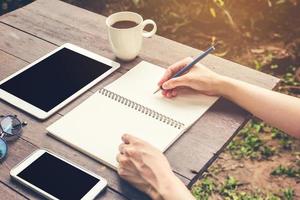 schließen oben Hand Frau Schreiben Notizbuch mit Bleistift auf Holz Tisch. Jahrgang getönt Filter. foto