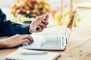 Asien Mann mit Telefon und Laptop auf Tabelle im Kaffee Geschäft mit Jahrgang getönt Filter. foto