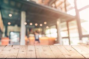 leeren Holz Tabelle und verschwommen Hintergrund Kunde beim Kaffee Geschäft verwischen Hintergrund mit Bokeh, Jahrgang getönt. foto